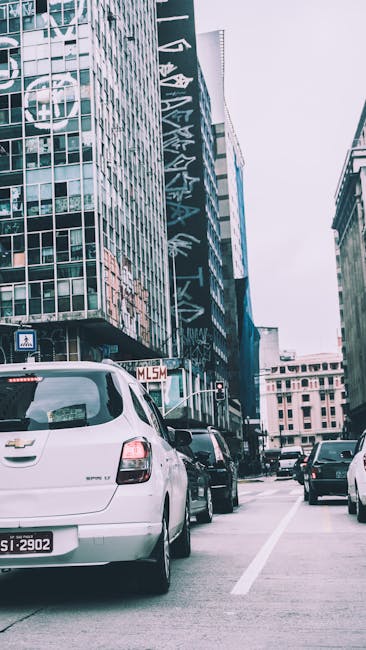 City street view with cars and modern skyscrapers in a bustling urban setting.