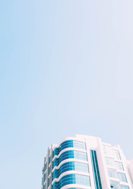 Low-angle view of a modern skyscraper with glass facade against a clear blue sky.